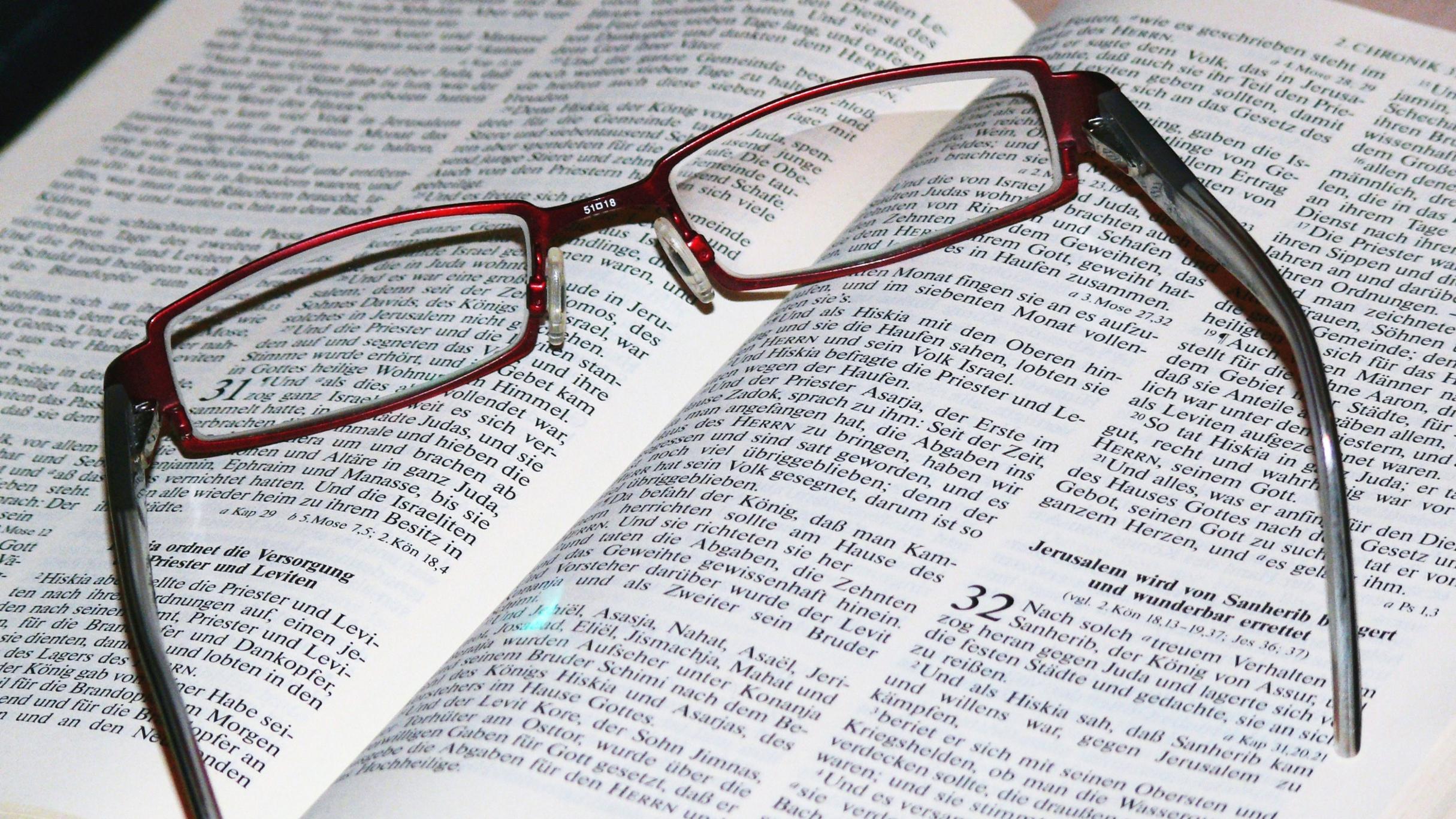 Auf einer aufgeschlagenen Bibel, Bibelstelle: Chronik 32, liegt eine dunkelrote Lesebrille.
