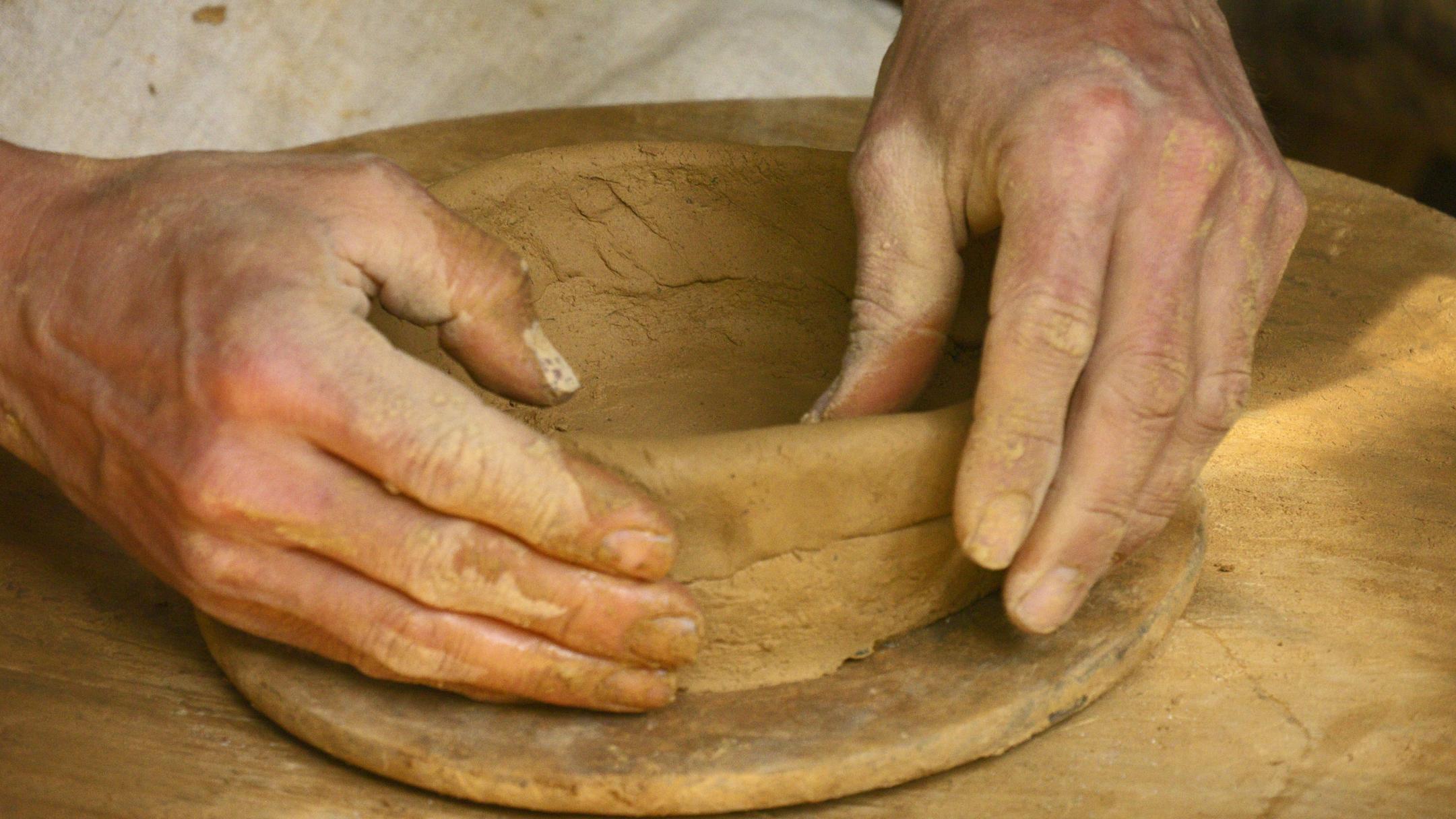 Zwei Hände bauen - Schicht für Schicht - eine Schale aus Ton auf.